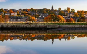 A-riverside-view-of-social-housing-in-West-Lothian-surrounded-by-autumn-trees-and-reflected-in-calm-water