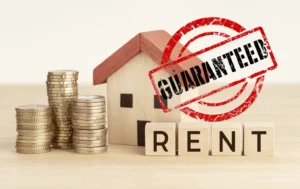 Stack-of-coins-beside-a-house-model-with-GUARANTEED-stamp-and-RENT-blocks