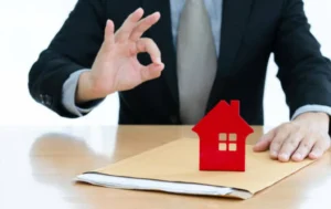 Business-professional-making-an-OK-gesture-with-a-red-house-model-symbolizing-Guaranteed-Rent-Solutions-for-Landlords
