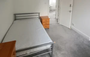 A-bedroom-in-supported-living-at-Charlotte-Road-Birmingham-featuring-a-metal-bed-frame-with-a-mattress-a-dresser-and-a-door-leading-to-another-room