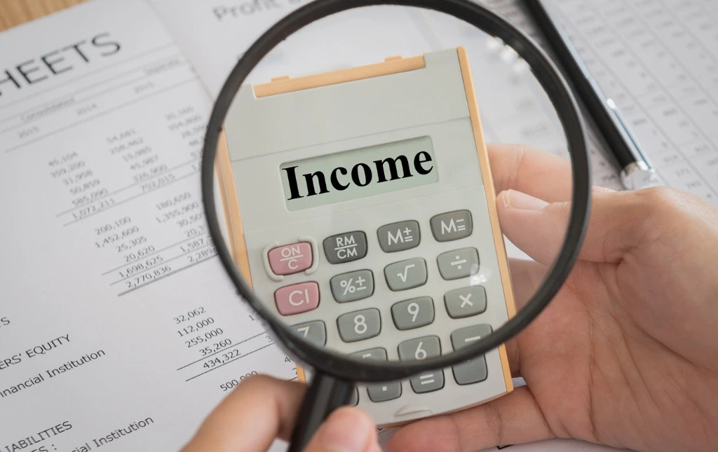 Magnifying-glass-focusing-on-Income-displayed-on-a-calculator-with-financial-documents-in-the-background