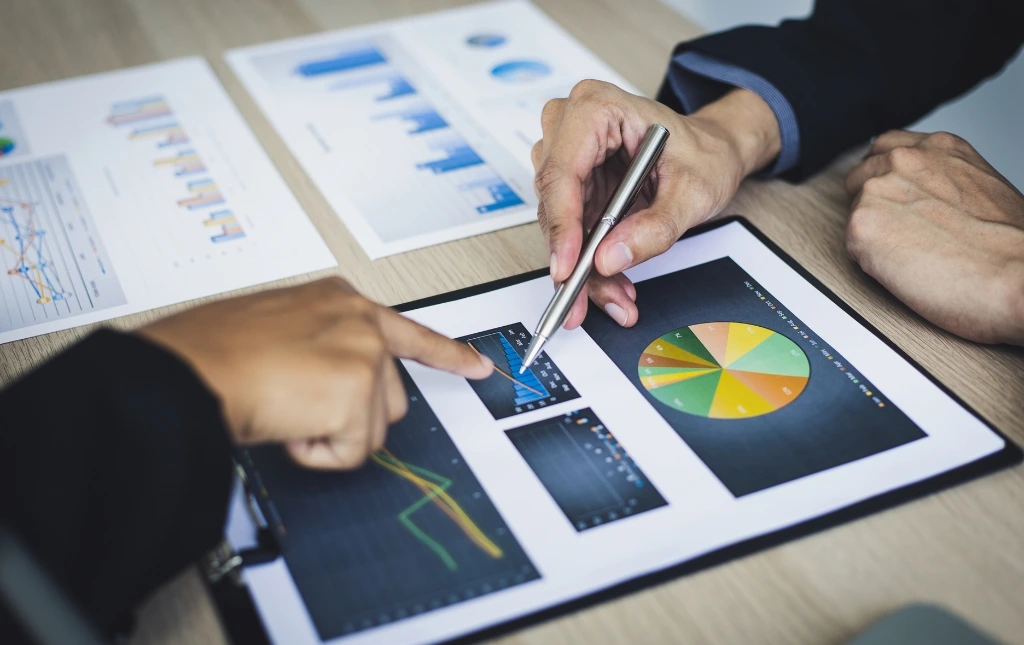 Two-people-analyzing-colorful-charts-and-graphs-on-paper-using-pens-during-a-business-meeting